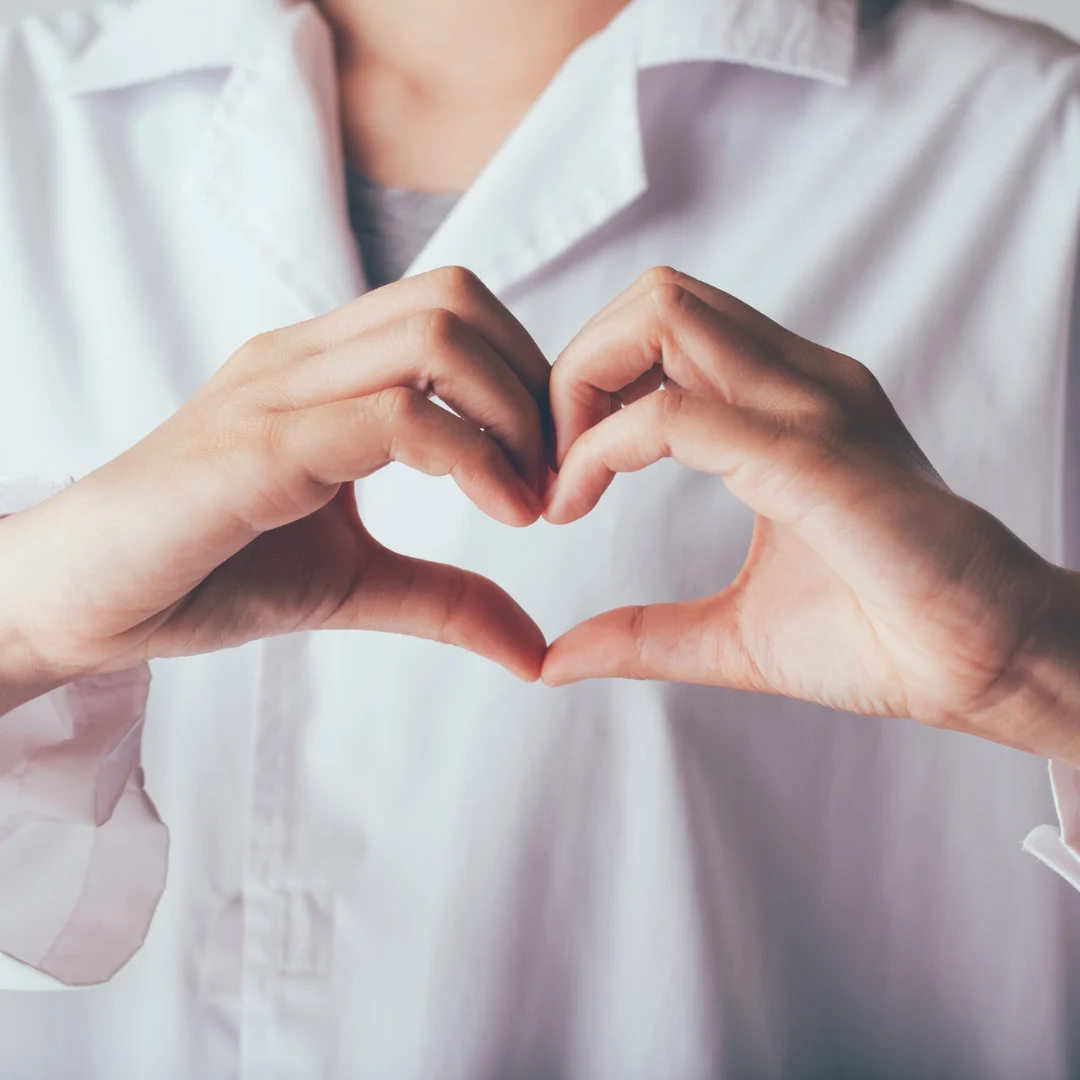 Healthcare professional forming a heart shape with hands to represent compassionate patient-centered care.